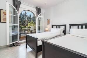 A hotel room with two beds, a balcony with a table and chairs, and a view of trees. - SAm24I- Cozy apartment walking distance to beach (Marbella)