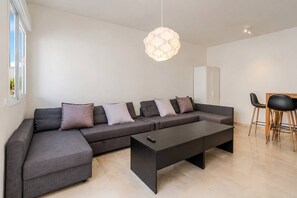 Ein modernes Wohnzimmer mit einer Eckcouch, einem Couchtisch und einem Essbereich mit Stühlen.