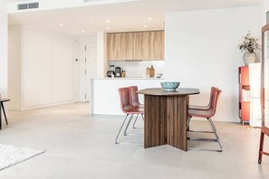 Een moderne keuken met witte kasten, een centraal eiland met zitplaatsen, en een eethoek met een ronde tafel en stoelen.