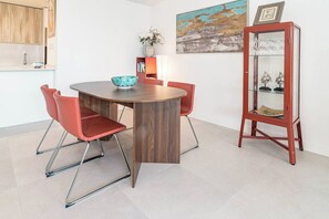 A dining area with a round wooden table, red chairs, a glass cabinet with decorative items, and a painting on the wall. - VV6-2B - Modern 2BR with large seaview balcony (Estepona)