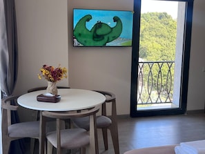 A room with a round table, a vase with flowers, a painting on the wall, and a balcony with a view of greenery. - Felic Home Stylish apartment overlooking the forest (Tsaghkadzor)