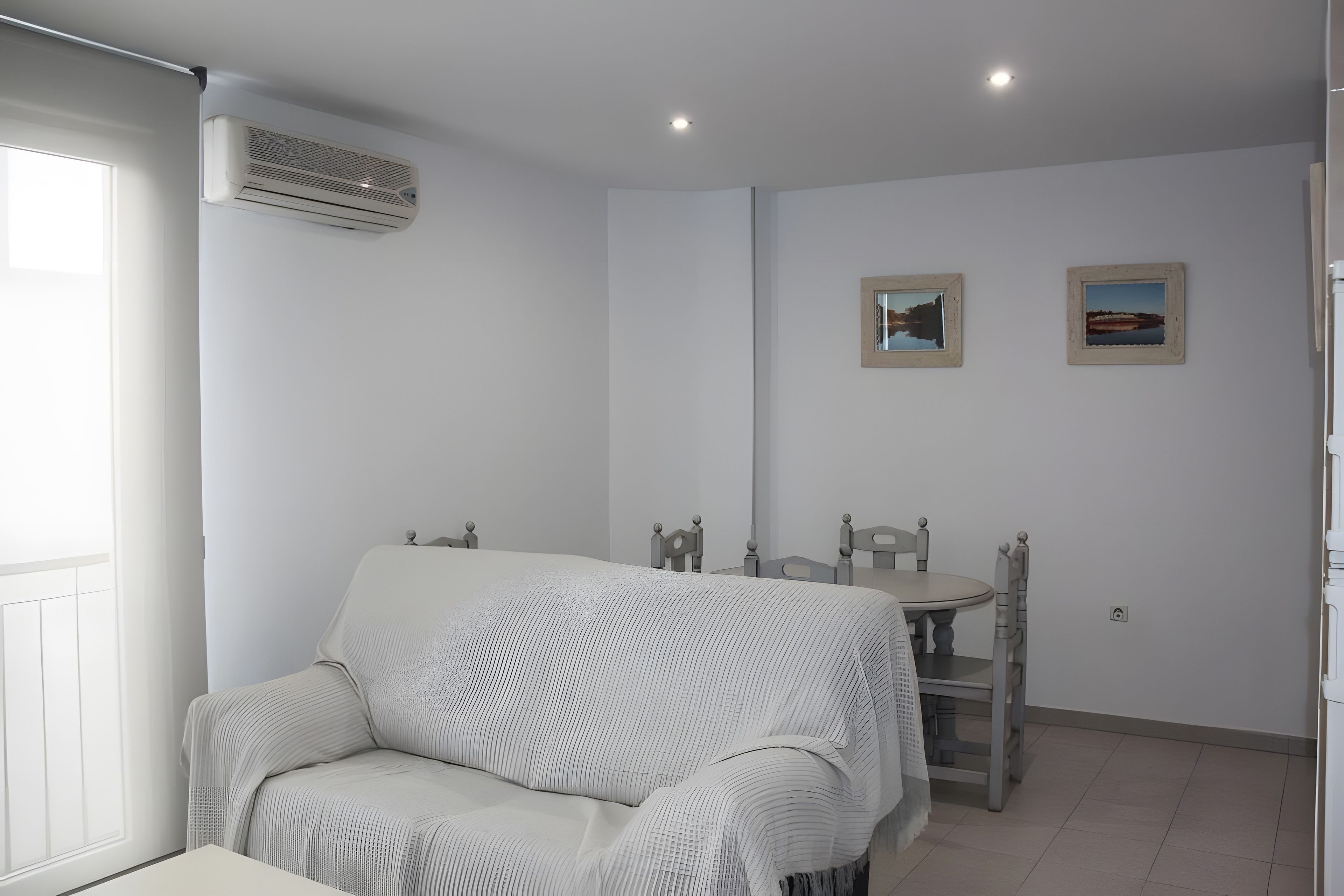 Ein modernes, minimalistisches Zimmer mit einer Couch, einem Esstisch mit Stühlen und zwei gerahmten Bildern an der Wand.