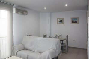 Ein modernes, minimalistisches Zimmer mit einer Couch, einem Esstisch mit Stühlen und zwei gerahmten Bildern an der Wand.