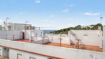 A rooftop terrace with a view of the sea, featuring white walls, red railings, and a brick floor.