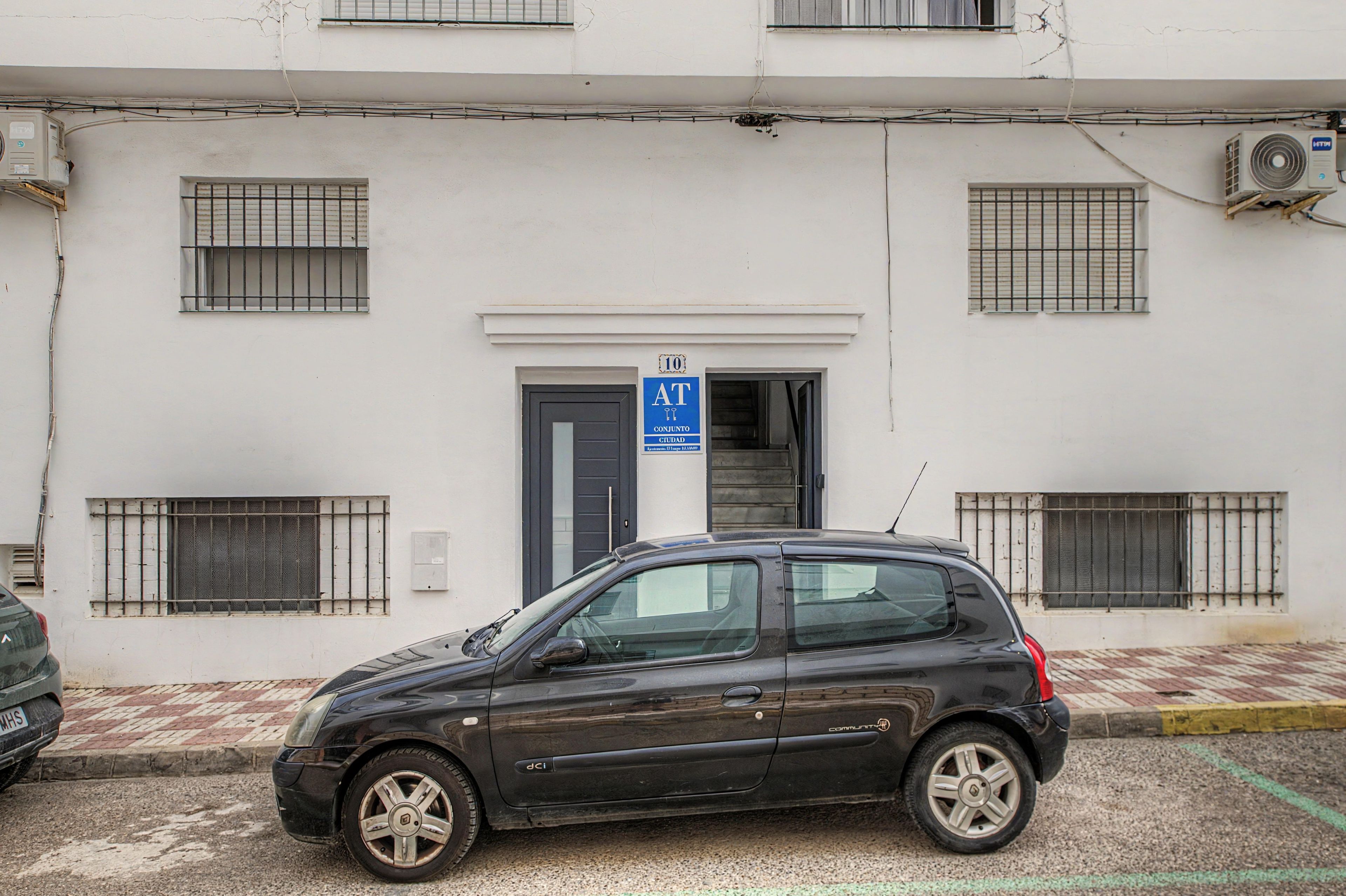 Ein Gebäude mit vergitterten Fenstern, einem blauen Schild, das eine öffentliche Toilette kennzeichnet, und einem parkenden Auto.