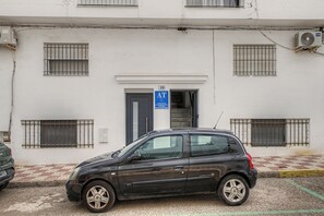 Ein Gebäude mit vergitterten Fenstern, einem blauen Schild, das eine öffentliche Toilette kennzeichnet, und einem parkenden Auto.