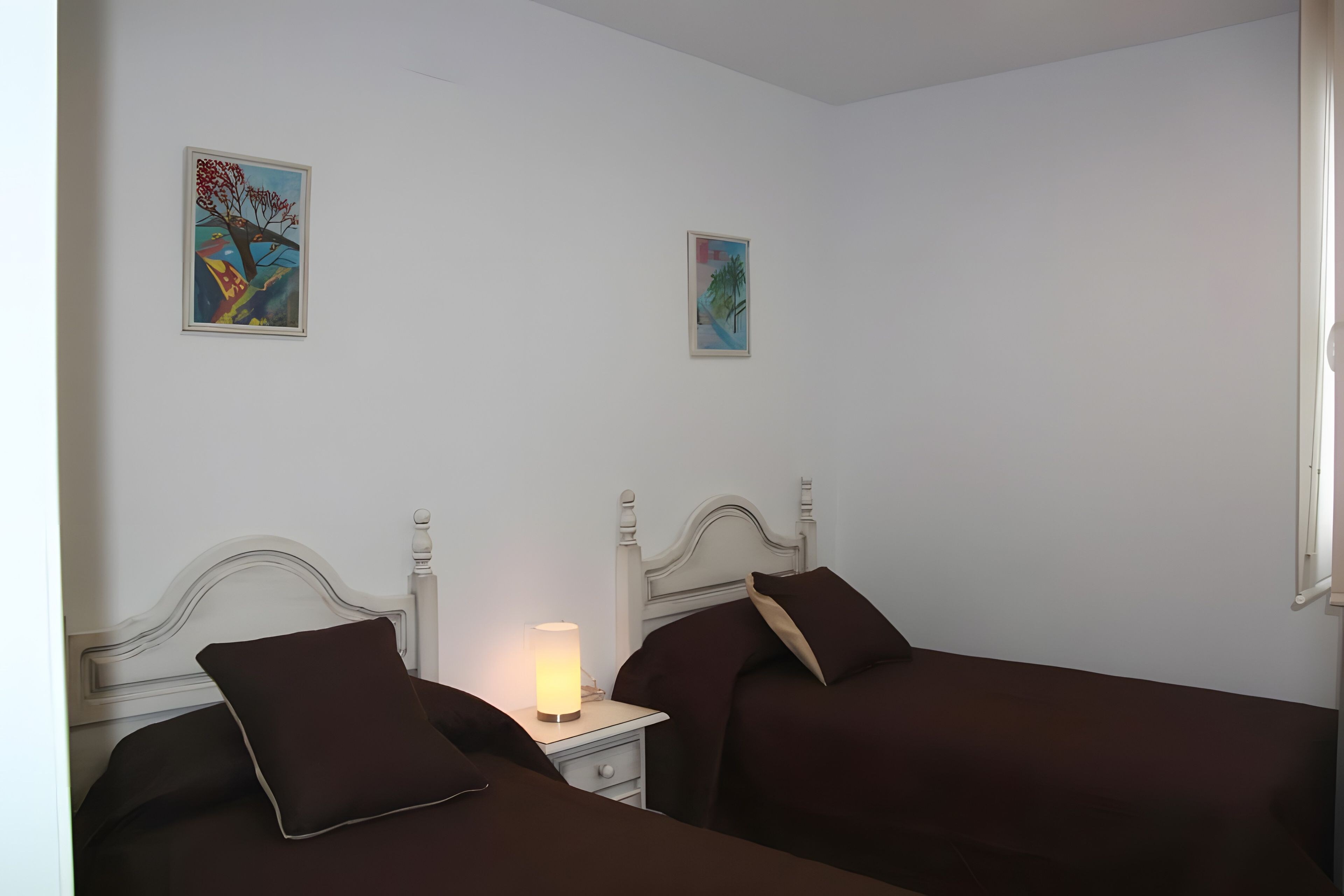 Ein Schlafzimmer mit zwei Betten, einem Nachttisch mit Lampe und zwei gerahmten Kunstwerken an der Wand.