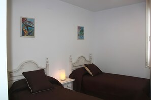 Ein Schlafzimmer mit zwei Betten, einem Nachttisch mit Lampe und zwei gerahmten Kunstwerken an der Wand.