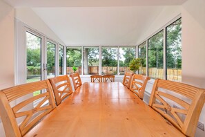 A dining area with a wooden table and chairs, large windows, and a view of a garden. - Newport Residence (Newport)