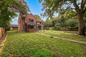 A residential backyard with a brick house, a lawn, a wooden fence, and a large tree. - Newport Residence (Newport)