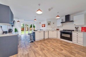 Una cocina moderna con gabinetes blancos, horno empotrado e iluminación colgante.