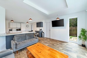 A modern kitchen with white cabinets, a grey sofa, and a wooden dining table. - Newport Residence (Newport)