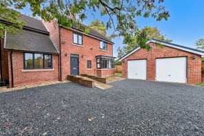 A residential property with a two-story brick house, a garage with two white doors, and a gravel driveway. - Newport Residence (Newport)