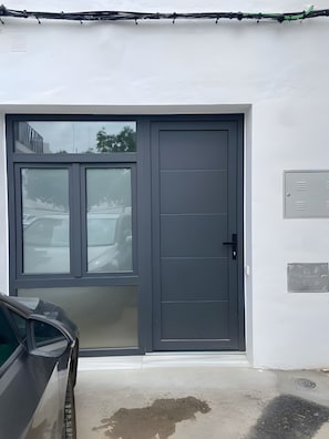 En garageindgang med en grå dør, en bil parkeret indeni og et metaludstyrsrum på væggen.