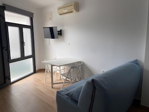 Et værelse med et hvidt bord, stole, en blå sofa, en skydedør af glas og en fastgjort aircondition.