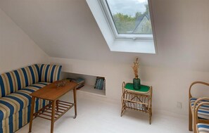A room with a sloped ceiling, a sofa, a small table, a wicker chair, and a view through a skylight. - 4 bedroom amazing home in søby ærø (Søby Ærø)