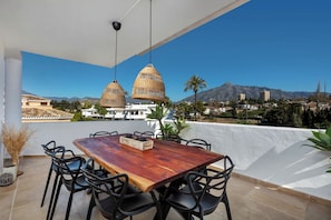 An outdoor dining area with a wooden table and chairs, overlooking a mountainous landscape. - MZa322A - Stylish penthouse with large terrace (Marbella)