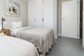 A bedroom with two beds, a wardrobe, a painting on the wall, and a nightstand with a lamp. - RDM9- Modern family apartment in Riviera del Mar (Mijas)