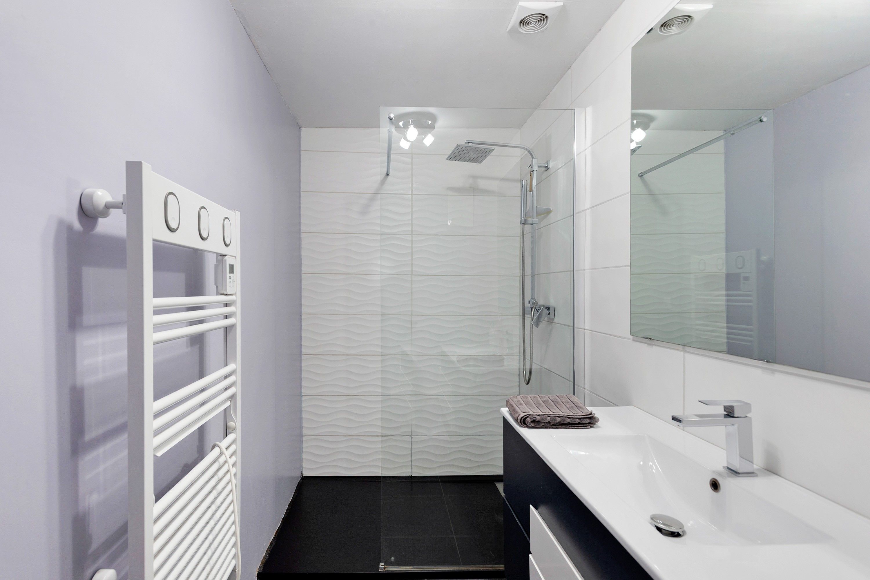 A modern bathroom with a glass shower enclosure, a white sink, and a towel on the counter.