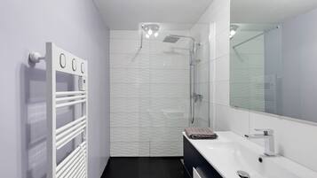 A modern bathroom with a glass shower enclosure, a white sink, and a towel on the counter.