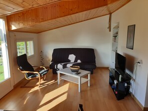Ein Wohnzimmer mit einem schwarzen Sofa, zwei schwarzen Sesseln, einem weißen Couchtisch und einem Fernseher.