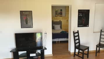 A living room with a flat-screen TV, a wooden floor, and a bed with a patterned bedspread.