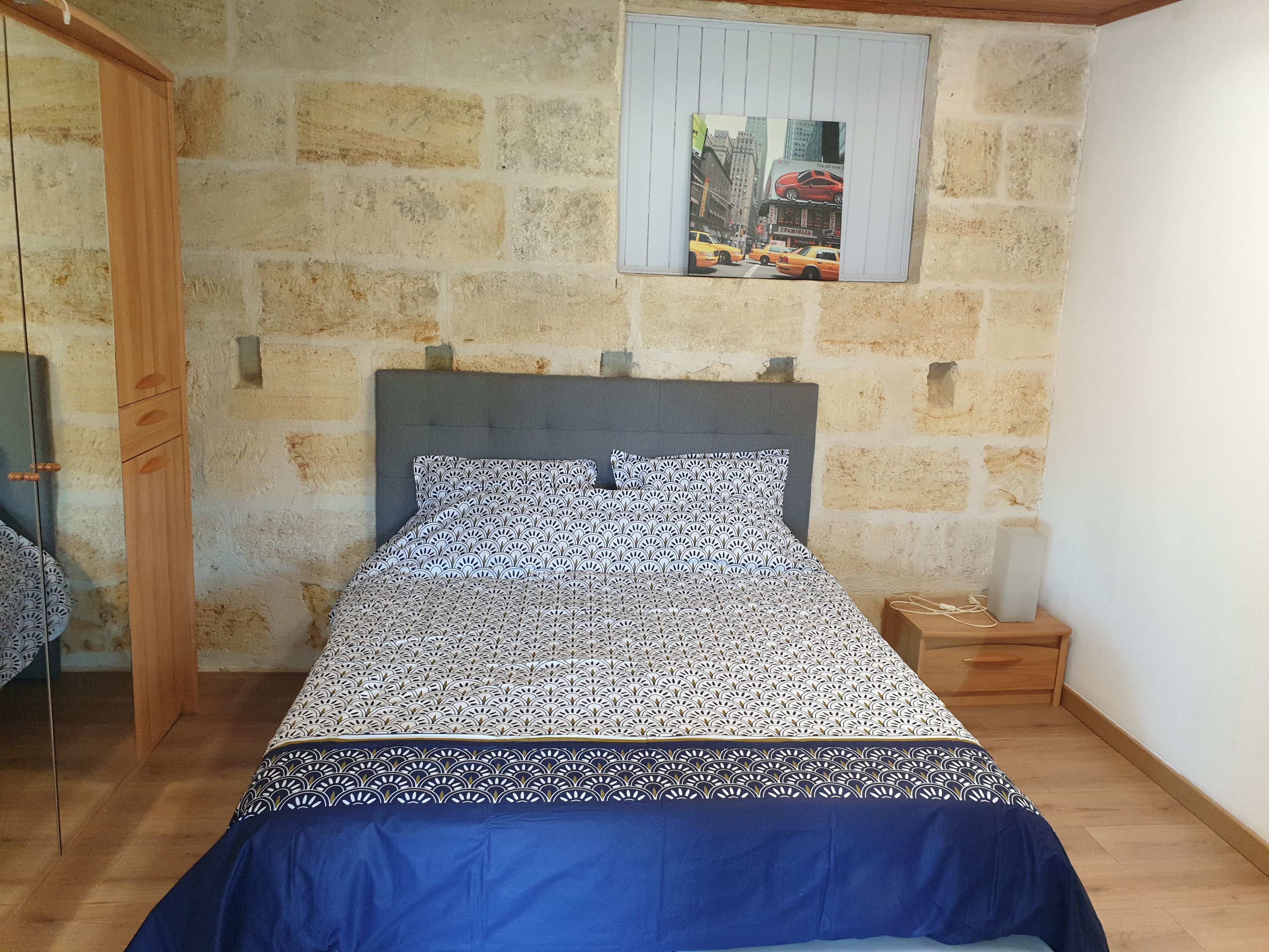 Ein Schlafzimmer mit Steinsandsteinwand, einem Bett mit gemusterten Bettbezügen, einem Nachttisch aus Holz und einem kleinen Tisch.