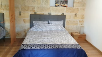 Ein Schlafzimmer mit Steinsandsteinwand, einem Bett mit gemusterten Bettbezügen, einem Nachttisch aus Holz und einem kleinen Tisch.