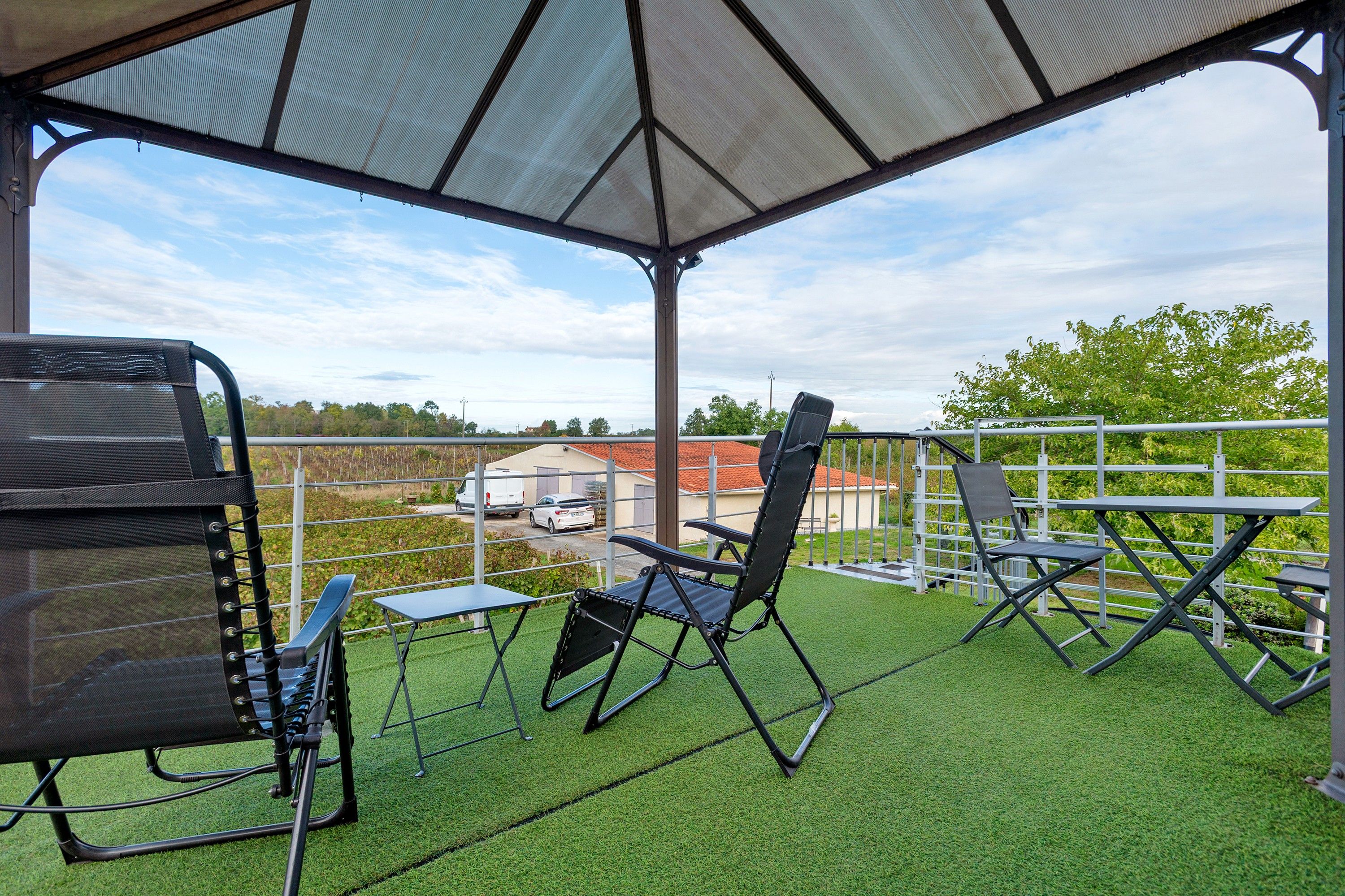An outdoor seating area with chairs and tables, a covered section, and a view of a building and vehicles in the background.