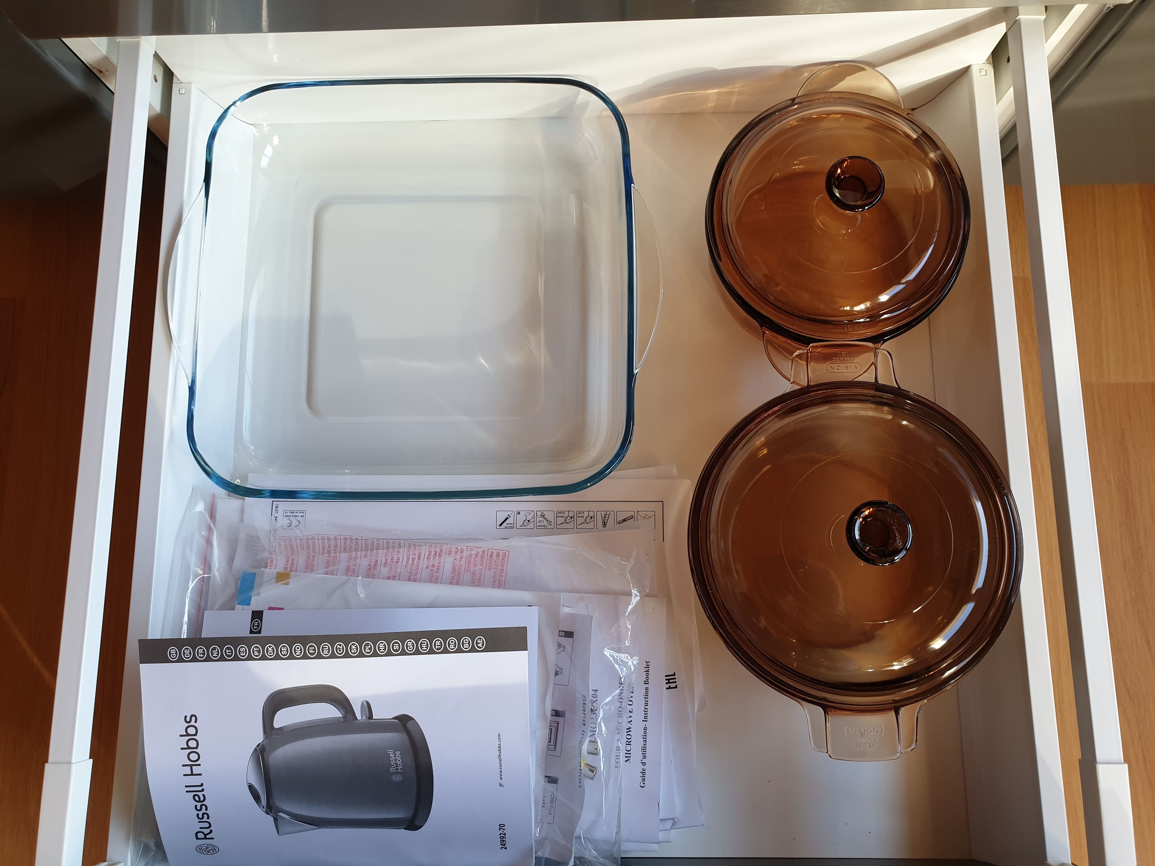 A drawer containing a glass storage container, a glass lid, and a booklet with instructions.