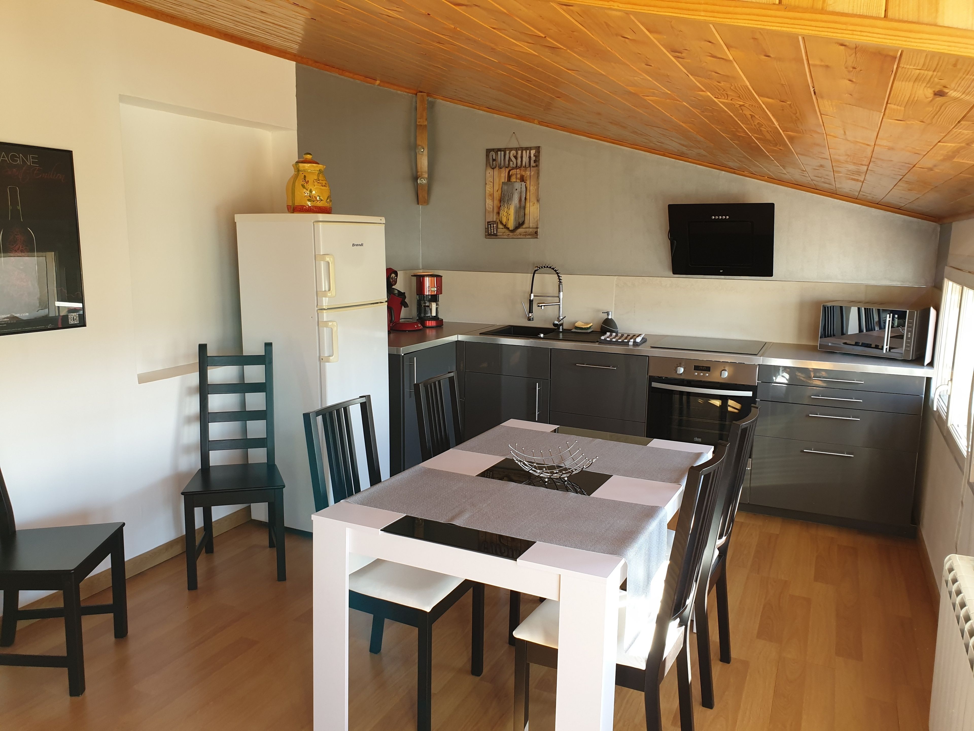 Eine kompakte Küche mit Kühlschrank, Kaffeemaschine und Mikrowelle. Es gibt einen Esstisch mit Stühlen sowie eine kleine Kücheninsel mit Spüle.