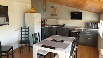 Eine kompakte Küche mit Kühlschrank, Kaffeemaschine und Mikrowelle. Es gibt einen Esstisch mit Stühlen sowie eine kleine Kücheninsel mit Spüle.