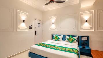 Quarto de hotel com cama, mesa de cabeceira, luminárias fixadas na parede e ventilador de teto.