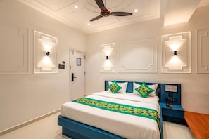 Una habitación de hotel con cama, mesita de noche, lámparas de pared y ventilador de techo.
