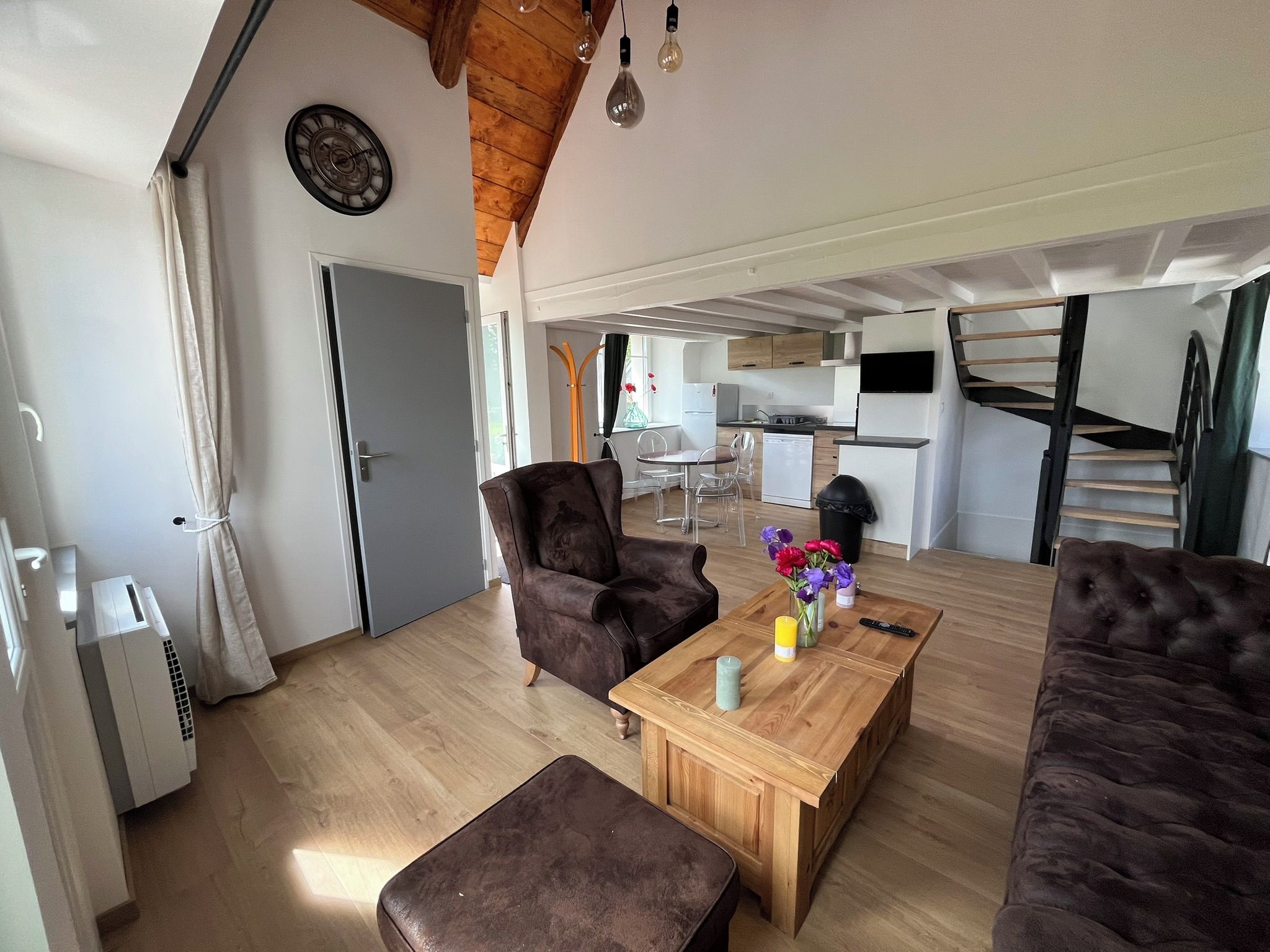 A modern living room with a sofa, armchair, and coffee table. A kitchen is visible in the background with a dining area.