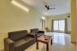 A living room with a sofa, a coffee table, a ceiling fan, and a large window with curtains. - Hotel O Metro Inn Manyata (Bengaluru)