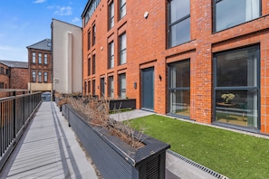 A modern building with red brick exterior, large windows, and a pathway with planters. - Luxury 4 Bed | Jewellery Quarter | Private Parking (Birmingham)