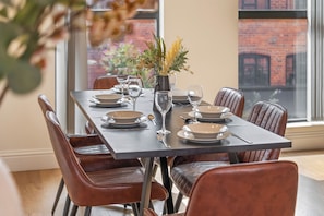 A dining table set for six with brown leather chairs, a vase with yellow flowers, and a view of a brick building through the window. - Luxury 4 Bed | Jewellery Quarter | Private Parking (Birmingham)