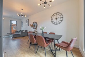 Una sala de estar moderna con comedor, destacando un reloj de pared grande, un sofá y una mesa de comedor con sillas.