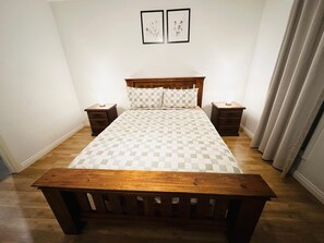 A bedroom with a wooden bed, two bedside tables, a checkered bedspread, and two framed pictures on the wall. - Modern 3 BR, 2 Bath, Free parking, WIFI, Step-free (Mansfield Park)