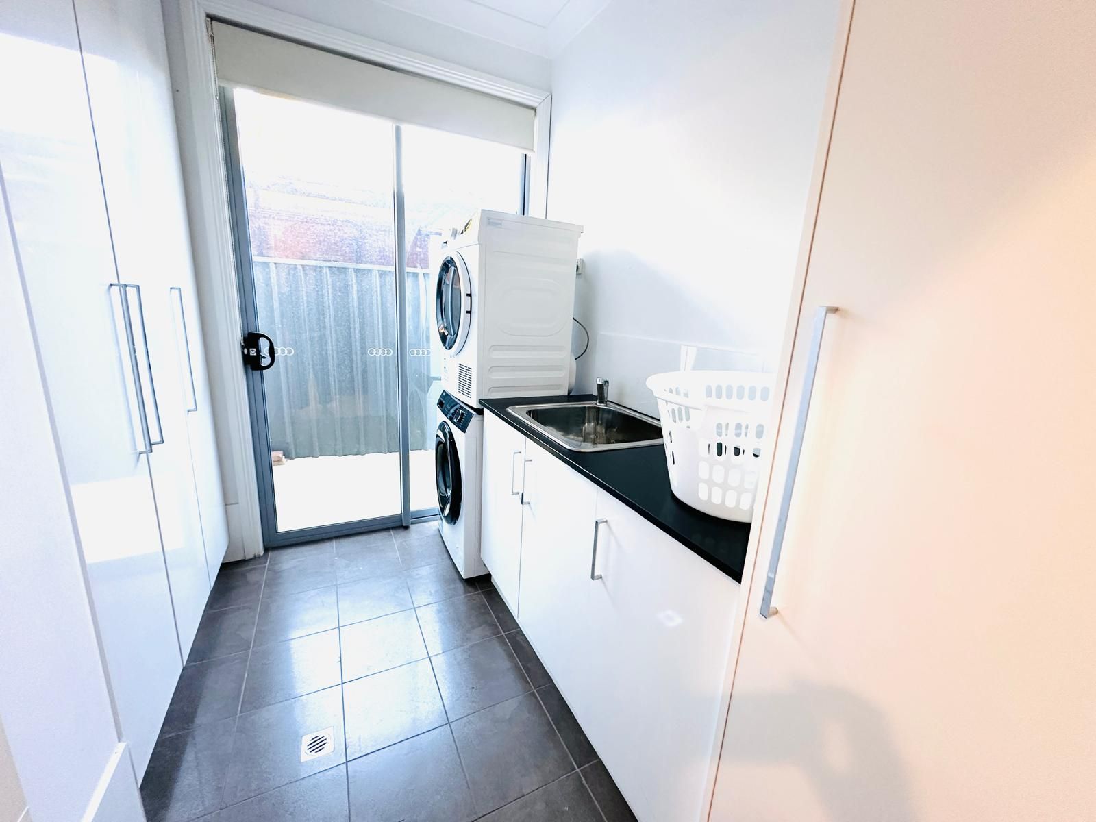 A laundry room with a washing machine, a dryer, a sink, and a laundry basket.
