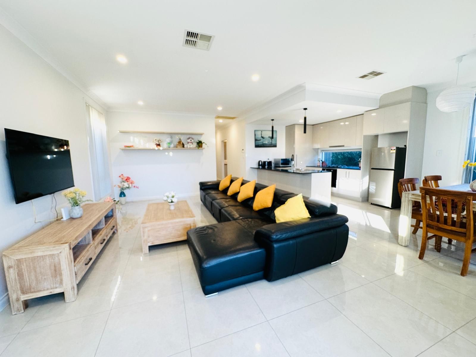A modern living room with a black leather sofa, wooden coffee table, and a flat-screen TV mounted on the wall.