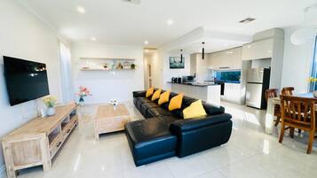 A modern living room with a black leather sofa, wooden coffee table, and a flat-screen TV mounted on the wall.