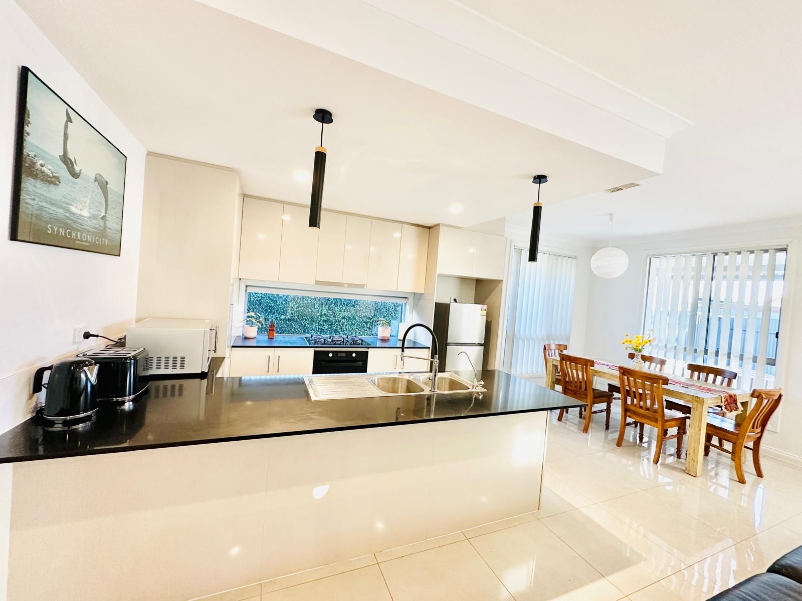 A modern kitchen with a central island, white cabinetry, and a dining area with wooden chairs.