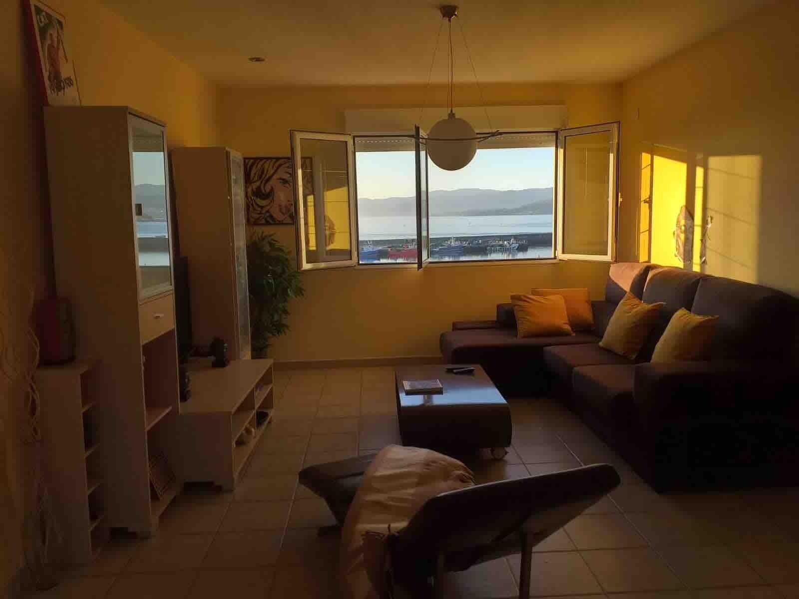 Un salon comprenant un canapé, une table basse, un téléviseur et une grande fenêtre donnant sur la mer.