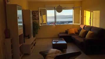 Un salon comprenant un canapé, une table basse, un téléviseur et une grande fenêtre donnant sur la mer.
