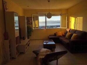 A living room with a sofa, a coffee table, a TV, and a large window with a view of the sea.