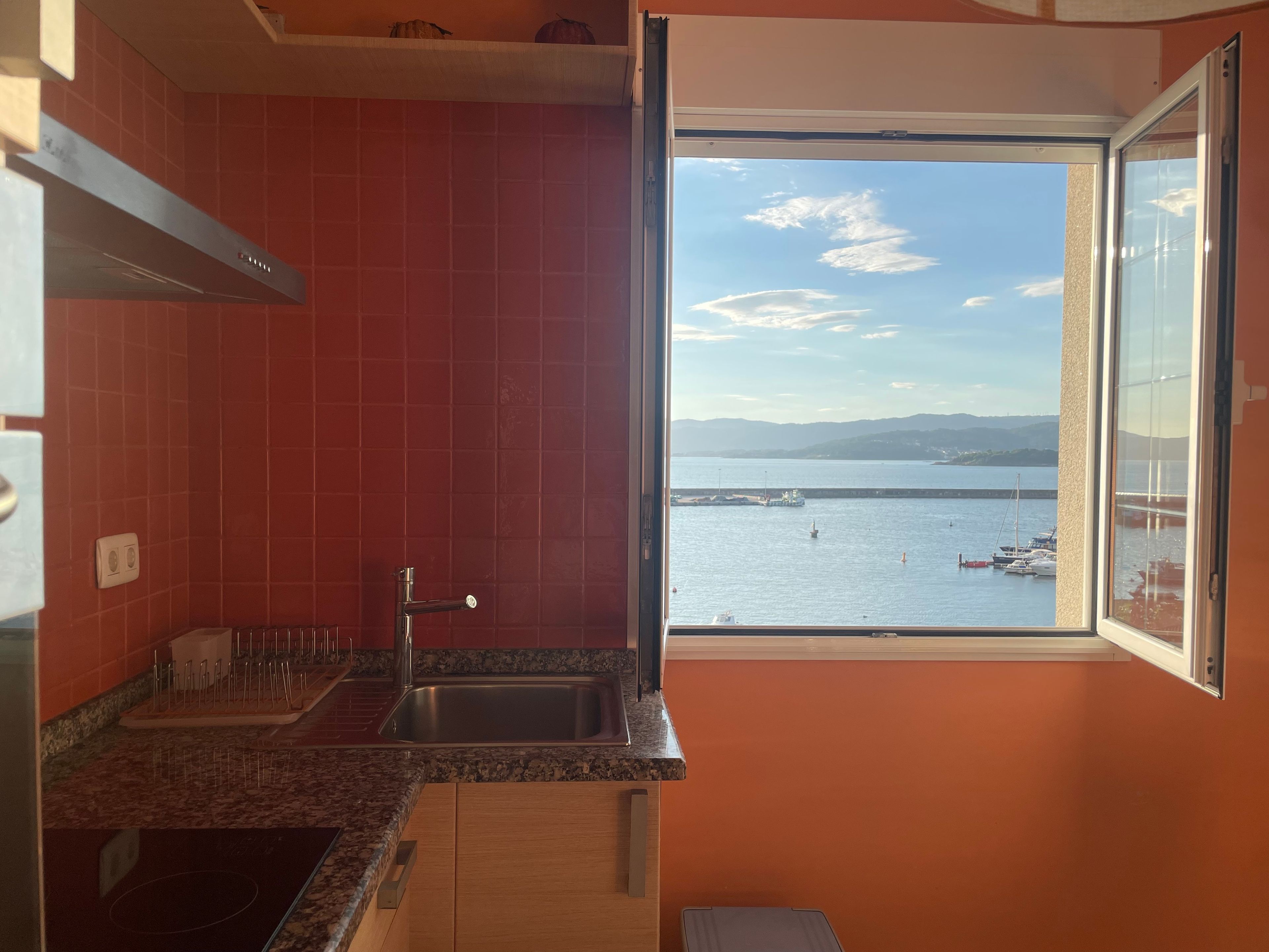 Una cocina con un ventanal grande, baldosas rojas y vista al mar.