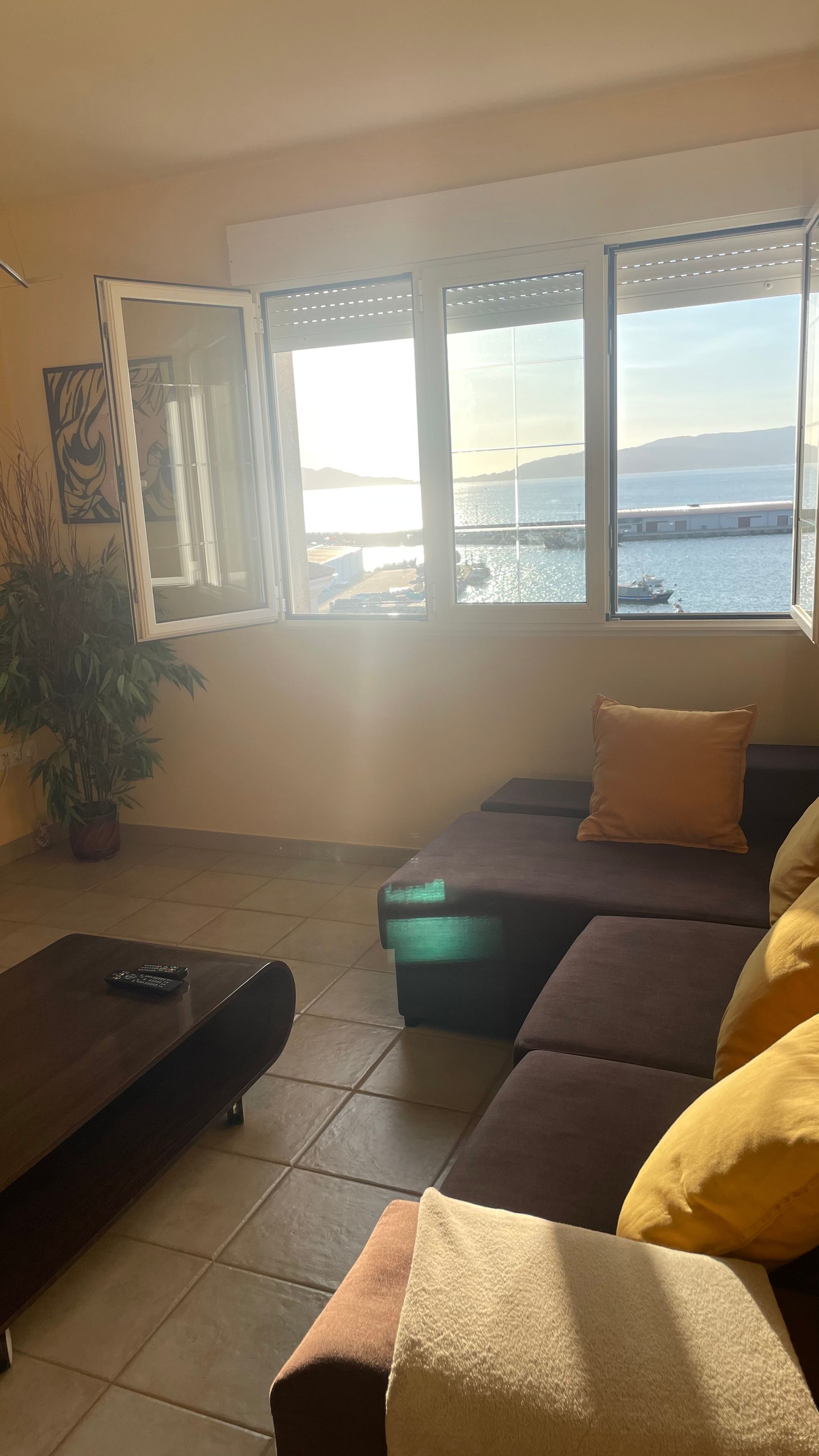 A living room with a sofa, a coffee table, and a large window with a view of the sea.
