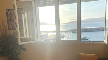 A living room with a sofa, a coffee table, and a large window with a view of the sea.